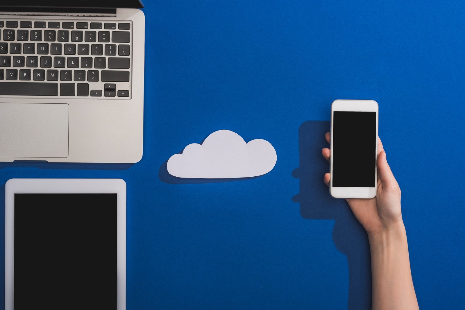 cropped view of woman holding smartphone near empty white paper cloud and laptop with digital tablet
