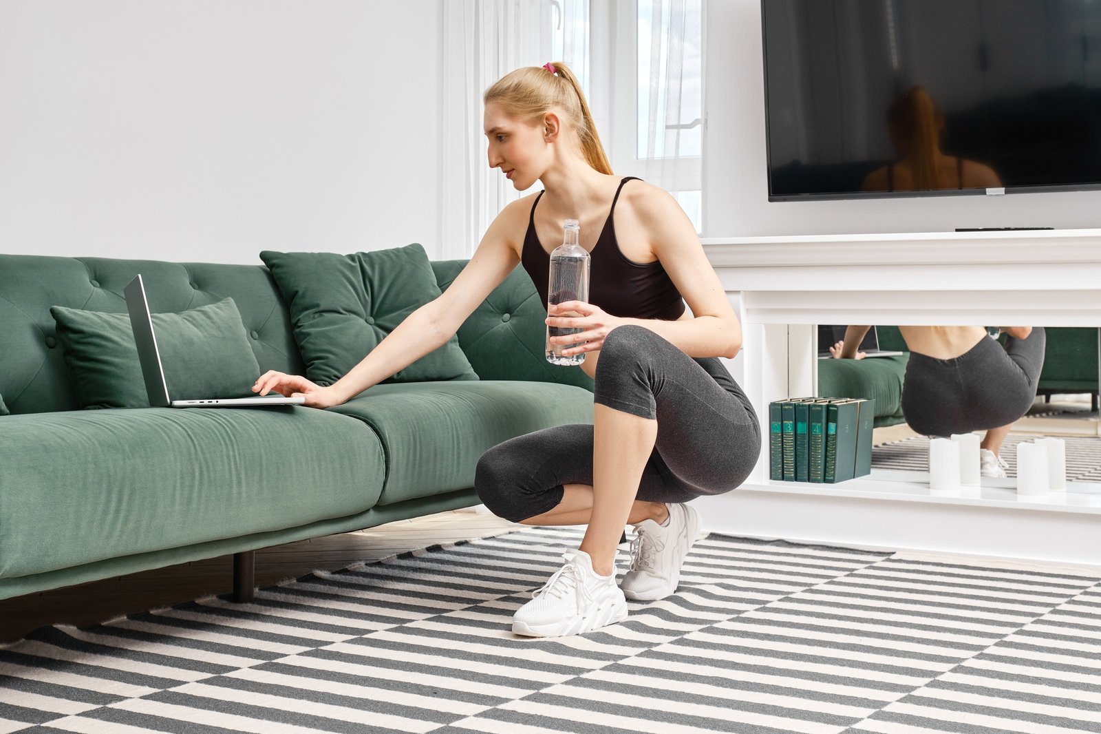 Active woman does training exercises at home and follows an online course video on laptop